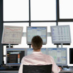 Rear view of stock trader looking at multiple computer screens